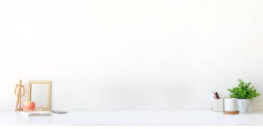 Comfortable workspace with picture frame, coffee cup, notebook and houseplant on white table. Copy space for your advertising text.