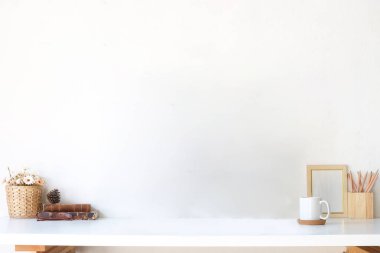 Resim çerçevesi, kitap, kahve fincanı ve kalem tutacağı beyaz masada. Reklam metnin için boşluk kopyala.