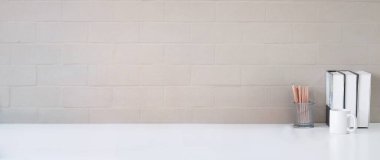 Bir fincan kahve, kitap ve kalem tutacağı beyaz masada, tuğla duvarlı. Reklam metnin için boşluk kopyala.