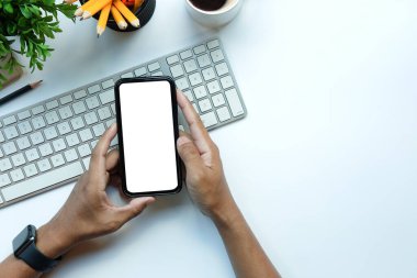 Beyaz ofis masasında boş ekranı olan akıllı telefonu tutan genç adam..