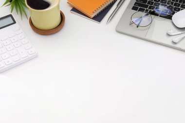 Bilgisayarı, bardakları, kahve fincanı ve defteri olan beyaz ofis masası. Üst görünüm.
