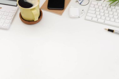 Bir fincan kahve, akıllı telefon, hesap makinesi ve beyaz ofis masasında kablosuz klavye..