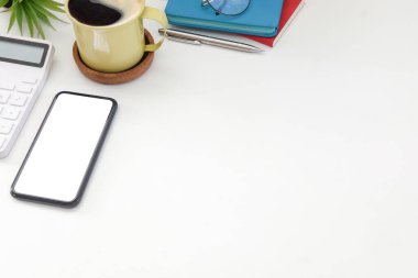 Akıllı telefon, kahve fincanı, hesap makinesi ve defterler beyaz masada..