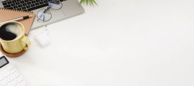 Bilgisayar laptopu, kahve fincanı, gözlük, hesap makinesi ve kablosuz kulaklık beyaz ofis masasında..