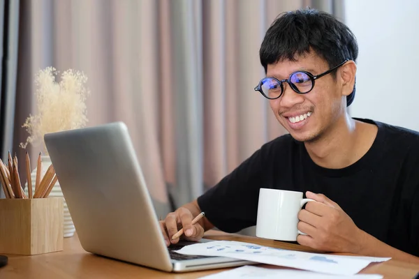 微笑着拿着咖啡杯和在家里使用笔记本电脑的亚洲人 — 图库照片