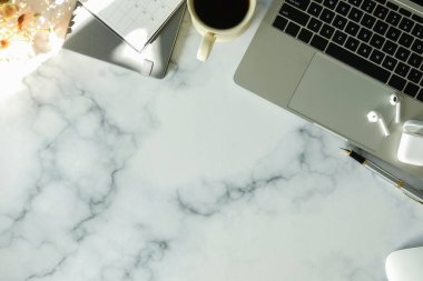 Laptop bilgisayar, kablosuz kulaklık, kahve fincanı ve mermer arka planda not defteri. Üst görünüm.