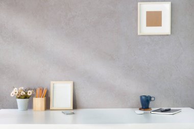 Resim çerçevesi, defter, kalem tutacağı, saksı ve kahve fincanı olan şık bir iş yeri..