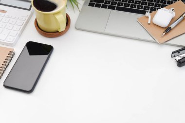 Akıllı telefon, bilgisayar dizüstü bilgisayar, kahve fincanı, defter ve hesap makinesi beyaz ofis masasında. Boşluğu kopyala.