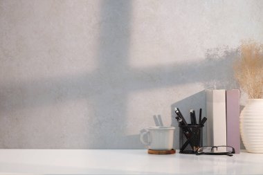 Bir fincan kahve, gözlük, kitap ve kalem tutacağı beyaz masada..