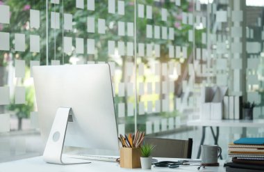 Bilgisayarlı iş yeri, kahve fincanı, kitaplar ve ofis malzemeleri beyaz masada..