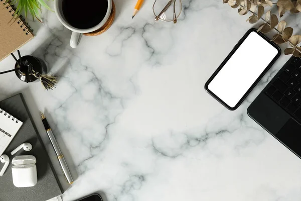 Üst görünüm akıllı telefon, kablosuz kulaklık, kahve fincanı ve mermer masadaki defter..