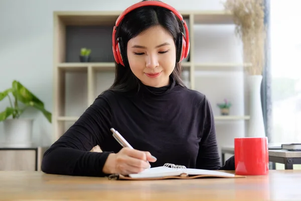 Досить Азіатська Жінка Слухає Музику Бездротовими Навушниками Пише Свій Щоденник — стокове фото
