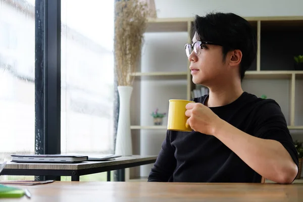 Thoughtful Young Asian Man Holding Coffee Cup Looking Out Window — Stock Photo, Image