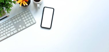 Akıllı telefon, kablosuz klavye ve kahve fincanı ile beyaz ofis masası..