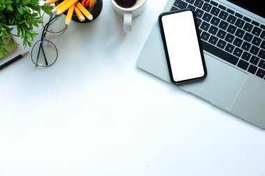 Akıllı telefon, dizüstü bilgisayar, kahve fincanı ve bardaklar beyaz masada. Düz yatıyordu.