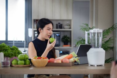 Çekici Asyalı kadın dijital tablette yemek tarifi arıyor ve mutfakta sağlıklı bir içecek hazırlıyor..