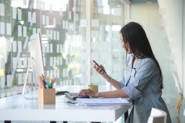 Güzel Asyalı iş kadını iş yerinde oturuyor ve akıllı telefon kullanıyor..