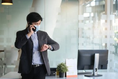 Yakışıklı işadamı cep telefonuyla konuşurken saati kontrol ediyor ve kol saatine bakıyor..