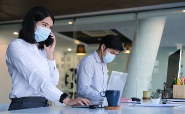 Koruyucu yüz maskesi takan iş adamları modern ofiste çalışıyor..