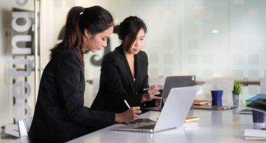 İki bayan iş arkadaşı toplantı odasında oturmuş iş stratejilerini tartışıyorlar..