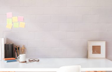 Yaratıcı iş yeri, boş çerçeve, kahve fincanı ve malzemeler beyaz masanın üzerinde renkli duvarlı yapışkan notlar.