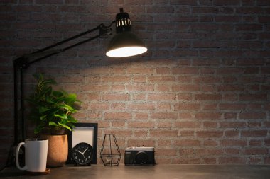 Kamera, resim çerçevesi, alarm saati ve tuğla duvarın önündeki beyaz masada saksı bitkisi olan yaratıcı bir iş yeri..