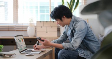 Yan görünüm milenyum adamı internette bilgi arıyor, oturma odasında bilgisayar laptopuyla çalışıyor.