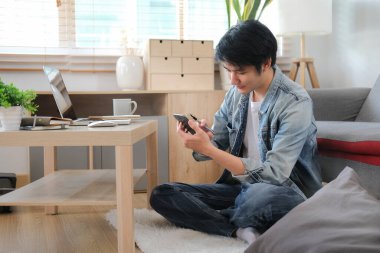 Mutlu genç adam sosyal medyayı kontrol ediyor ya da akıllı telefondan alışveriş yapıyor..