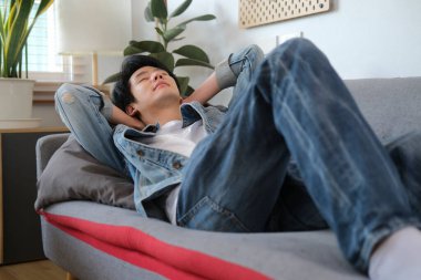 Memnuniyet duyan Asyalı genç adam ellerini başının arkasına koyup evdeki kanepede dinleniyor..