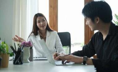 İş arkadaşları onu dinlerken kendine güvenen bir iş kadını gülümseyerek bir şeyler söylüyor ve tartışıyor..