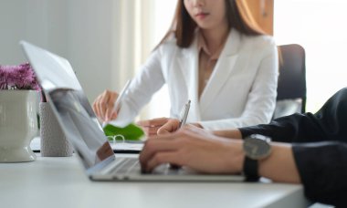 Çalışan iş arkadaşlarıyla birlikte otururken dizüstü bilgisayarda yazı yazan kırpılmış işadamı elleri.