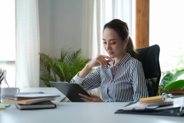 Düşünceli bayan girişimci modern ofiste oturuyor ve mali raporları kontrol ediyor..
