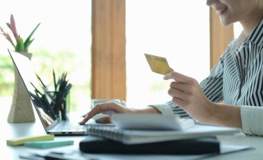 Elinde kredi kartı tutan ve hesap makinesi kullanan gülümseyen genç Asyalı kadın. Çevrimiçi alışveriş, e-ticaret, internet bankacılığı kavramı.