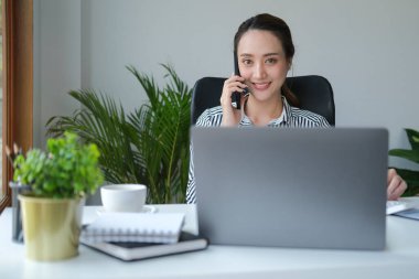 Dizüstü bilgisayar kullanan ve iş ortağıyla cep telefonuyla konuşan kendine güvenen genç bir iş kadını..
