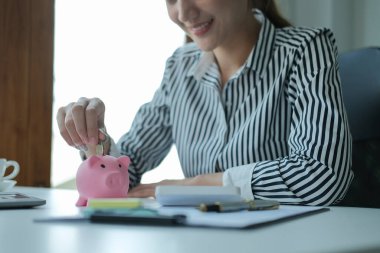 Gülümseyen iş kadını elini kumbaraya para koyuyor. Gelecek için para biriktirmek, iş yatırımları finansman muhasebesi.