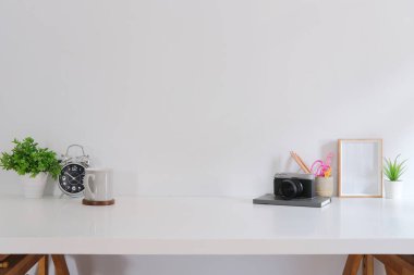 Kameralı ofis masası, saksı bitkisi, kahve fincanı, kırtasiye ve resim çerçevesi beyaz masada.. 