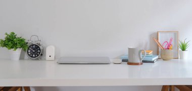 Dizüstü bilgisayarı, kırtasiyesi, resim çerçevesi ve saksı bitkisi olan rahat bir iş yeri.