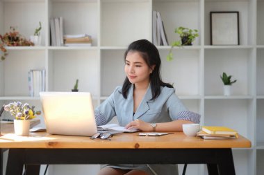 Confident asian business woman using computer tablet while sitting in bright modern office.	