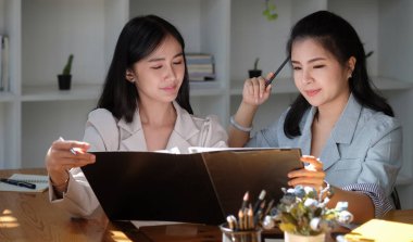 İki bayan iş arkadaşı parlak ofiste bazı evrak işlerini tartışıyorlar..