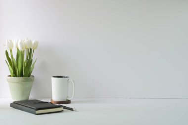 Tencerede beyaz lale buketi, kahve fincanı ve defter olan en az iş yeri. Metin veya bilgi içeriği için alanı kopyala.
