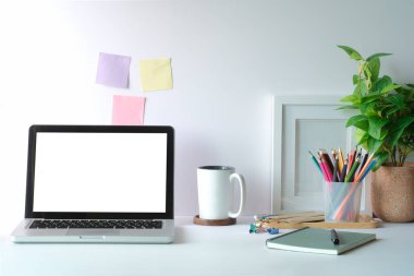 Laptop, kahve fincanı, saksı bitkisi ve beyaz masa üzerindeki kırtasiye malzemeleriyle rahat bir çalışma alanı. Merkez Ofis.