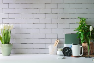 Çiçek saksısı, kahve fincanı ve beyaz masa üzerine kırtasiye malzemesi olan şık bir iş yeri. Merkez ofis. Metin ve bilgi içeriği için alanı kopyala.