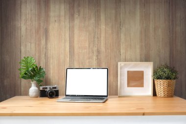Home workspace laptop computer, coffee cup, potted plan and camera on wooden table.	