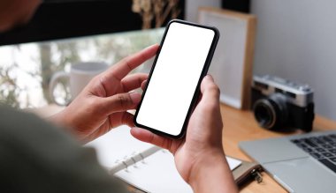 View Man Freelancer 'ı kapat. Ofis masasında oturuyor ve akıllı telefon kullanıyor. Metin veya bilgi içeriği için boş ekran.