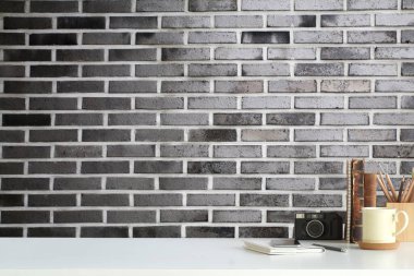 Retro kamerası, kahve fincanı ve tuğla duvarlı beyaz masa üzerinde kırtasiyesi olan yaratıcı bir iş yeri. Merkez, kopyalama alanı.