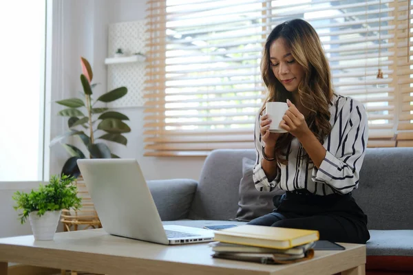 Rahat genç bir kadın, parlak oturma odasında koltukta oturuyor ve kahve içiyor..