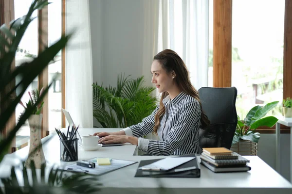 明るい現代オフィスでコンピュータのラップトップで働く集中ビジネス女性の側面図 — ストック写真
