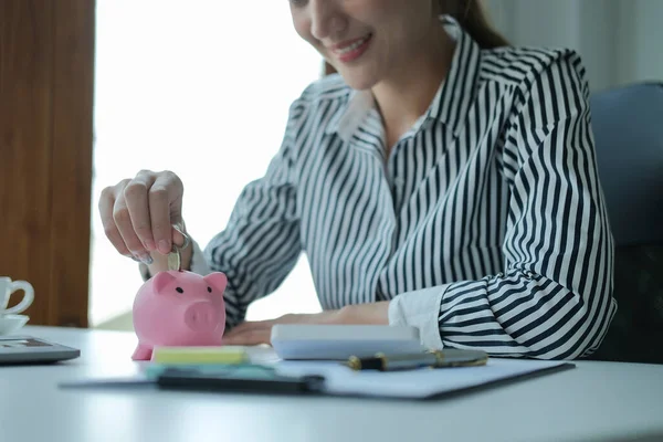 Gülümseyen iş kadını elini kumbaraya para koyuyor. Gelecek için para biriktirmek, iş yatırımları finansman muhasebesi.