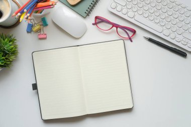 Düz dizüstü bilgisayar, gözlük, kahve fincanı ve saksı çiçeği beyaz ofis masasının üzerinde..