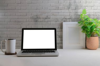 Ofis masası, dizüstü bilgisayar, kahve fincanı, saksı ve tuğla duvarlı resim çerçevesi..